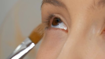 A professional artist makes make-up to a beautiful girl model, feathering powder, highlighter, foundation cream with a special brush for makeup