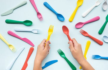 Top view of hand holding colorful spoon and fork with another element on color table