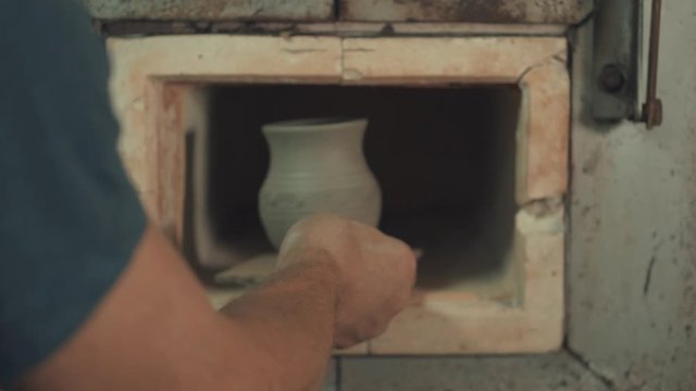 Man use a clay oven. Oven for clay. Man pust a jug inside