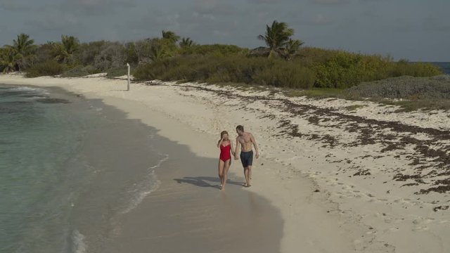 Aerial view of happy couple holding hands and walking on beach / Petit Tabac, Tobago Cays, St. Vincent and the Grenadines