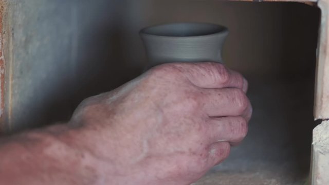 Man use a clay oven. Oven for clay. Man pust a jug inside