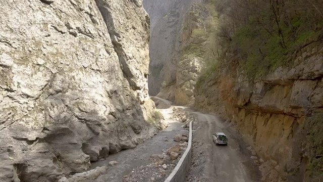Drone Follow Footage Of White SUV Driving Through Steep Canyon On Gravel Road