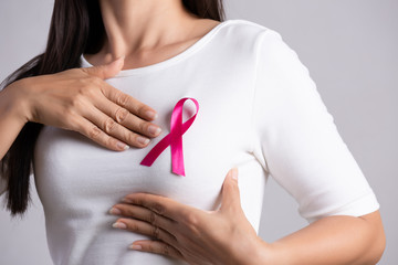 Closeup of pink badge ribbon on woman chest to support breast cancer cause. Healthcare, medicine...