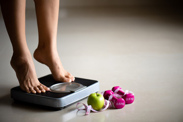 Female leg stepping on weigh scales with measuring tape and green apple. Healthy lifestyle, food and sport concept. - obrazy, fototapety, plakaty