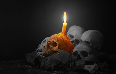 Orange Skull with candle light on pile of skulls and bone on old wood background on black and white tone/ different concept..