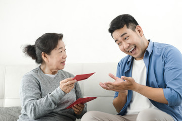 Happy Asian mother give red envelopes containing cash to her son for Chinese New Year concept.