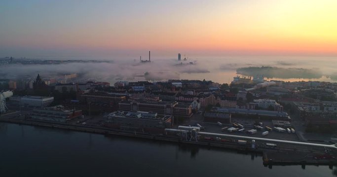 Helsinki foggy dusk, Aerial, tracking, drone shot, of Katajanokka, korkeasaari,tervasaari and fog clouds and colorful sky, at the baltic sea, on a sunny and autumn morning, in Helsingfors, Finland
