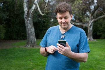 Fototapeta premium A man plays an augmented reality game on his mobile phone in a park in Christchurch, New Zealand