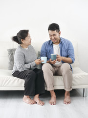 Asian mother and her son talking and drinking at home, lifestyle concept.