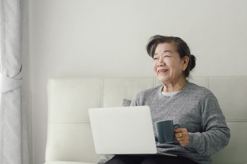 Asian senior woman using laptop at home, lifestyle concept.