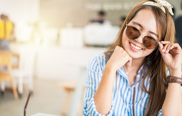 Beautiful young Asia woman with sunglasses and just smile in coffee shop with copy space.