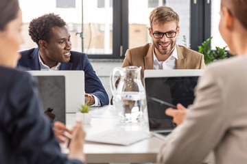 selective focus of multiethnic businesspeople sitting at tables during conference in office