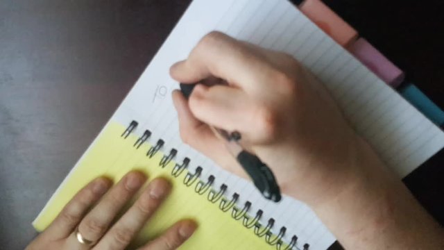 Adult white Caucasian male with a partially amputated left hand index finger  writing a to do list on a lined A5 spiral note book.