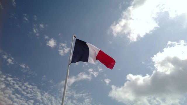 French flag sways in the wind. Blue sky with scattered clouds in the background.