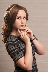 Close-up of a brown-haired girl with make-up and hairstyle holding hands near her face.