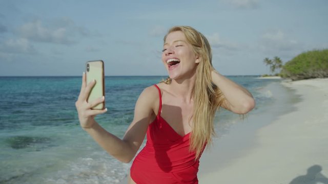 Woman standing on ocean beach posing for cell phone selfies / Petit Tabac, Tobago Cays, St. Vincent and the Grenadines