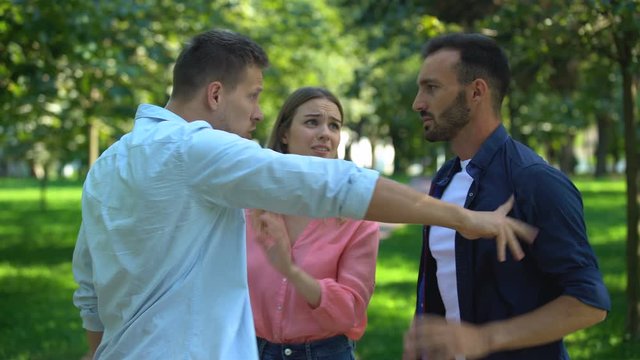Frightened woman standing between fighting men, rivalry for girls attention