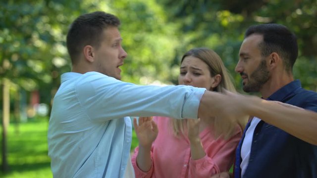 Worried woman trying to stop jealous boyfriend fighting with another man