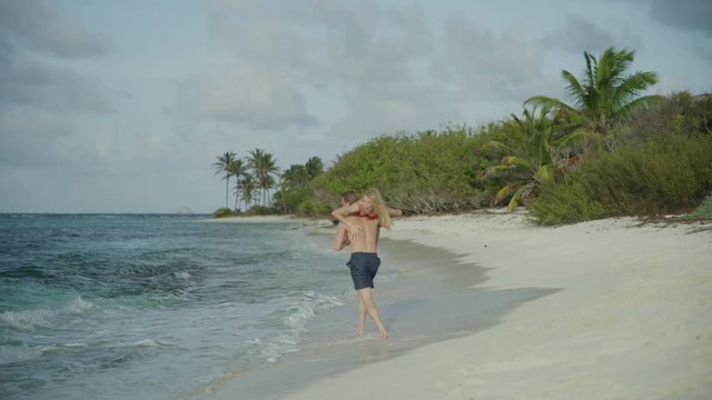 Man chasing and catching woman on beach then carrying her into ocean / Petit Tabac, Tobago Cays, St. Vincent and the Grenadines