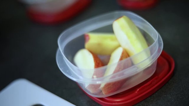 Slow Motion Shot of someone putting freshly cut apple slices into a small Tupperware container.