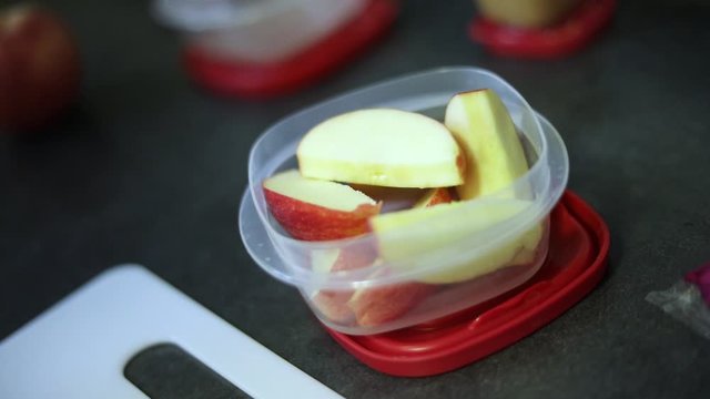 Slow Motion Shot of someone putting freshly cut apple slices into a small Tupperware container.