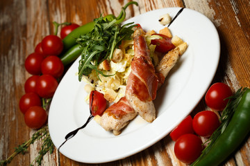 Caesar salad with chicken and bacon on wooden table