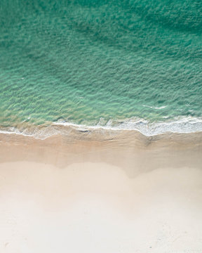 Vertical aerial of a beach at sunrise with nice white sand, blue turquoise ocean on the west coast for a holiday destination.
