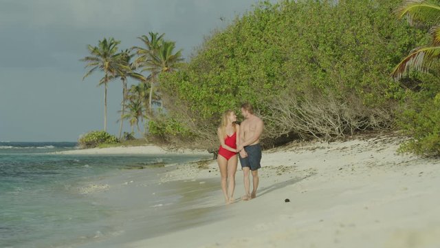 Slow motion of happy romantic couple holding hands and walking on beach / Petit Tabac, Tobago Cays, St. Vincent and the Grenadines