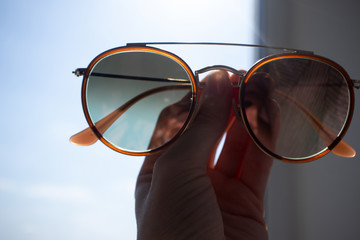 Elegant sunglasses in female hand in front of  window