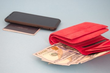 Red wallet with dollar banknotes, mobile phone and passport against the blue background