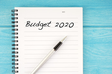 Budget 2020 wording written on a notebook with a pen and over the blue wooden surface
