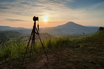 Mountain view silhouette a camera on tripod with yellow sun light and cloudy sky background, sunrise at Khao Takhian (Takian) Ngo, Khao Kho, Phetchabun, Thailand.