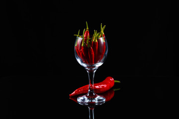 Red chili peppers in a glass on a glass table on a dark background.