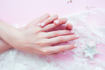 woman hands with manicure among white lace on pink background, cosmetic concept