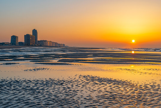 The beach of Ostend city at sunset with unsharp foreground by the North Sea with the urban skyline of sea view apartments, West Flanders, Belgium.