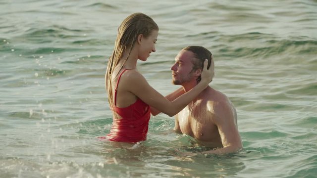 Romantic couple swimming and kissing in ocean waves / Petit Tabac, Tobago Cays, St. Vincent and the Grenadines