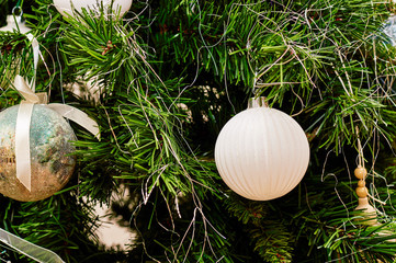 bright green Christmas spruce branch with glass decorative ball toys and tape in white and blue colors. toys are hanging on the branches for the new year holiday