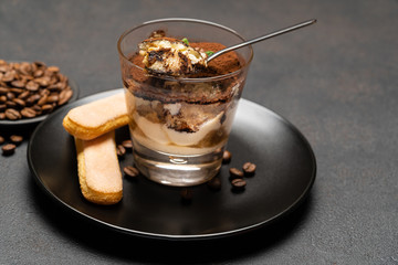 Portion of Classic tiramisu dessert in a glass cup on dark concrete background