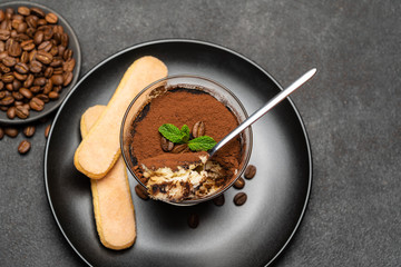 Portion of Classic tiramisu dessert in a glass cup on dark concrete background