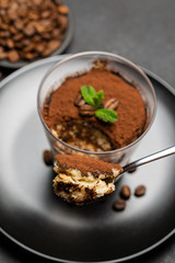 Portion of Classic tiramisu dessert in a glass cup on dark concrete background