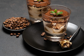 Portion of Classic tiramisu dessert in a glass cup on dark concrete background