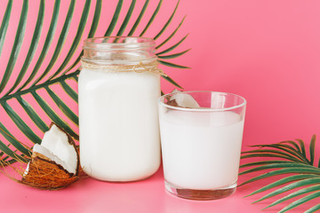 Cracked coco and coconut milk in glass on bright pink background