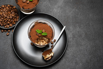 Portion of Classic tiramisu dessert in a glass cup on dark concrete background