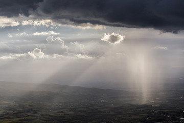 Naklejka na ściany i meble Sunray shines through clouds and rain over the mountains in the middle of shadows