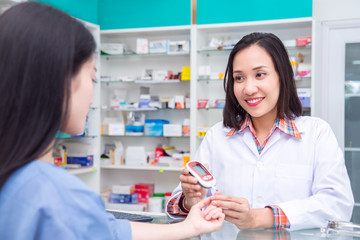 Beautiful asian Pharmacist checking patient blood sugar by glucometer in drugstore