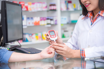 Hands of Pharmacist checking patient blood sugar by glucometer in drugstore