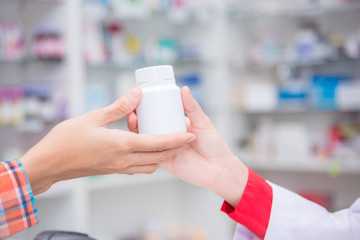 Hand of pharmacist giving a bottle of medicine to patient in drugstore