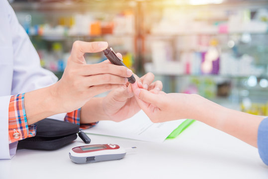 Hands of  Pharmacist checking patient blood sugar by glucometer in drugstore