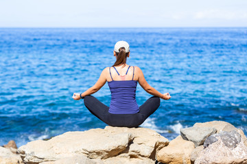 Young woman relaxing in yoga pose near the ocean