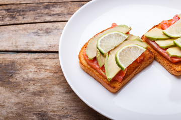 Fresh salmon sandwich with avocado and lime on white plate